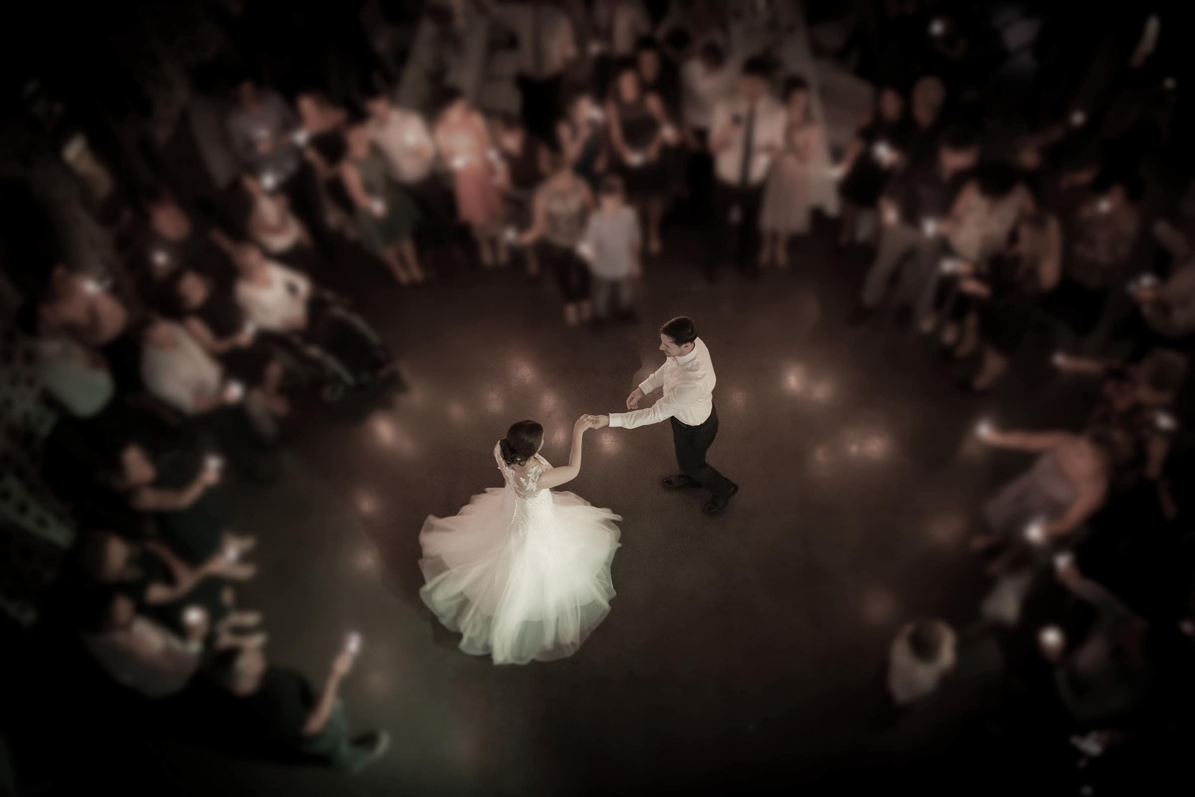 Bride in a white gown dancing with the groom while guests watch from around the floor