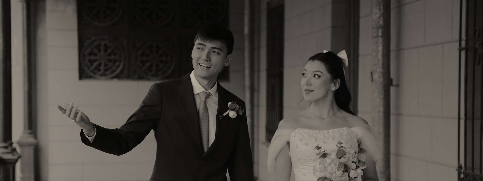 Groom gesturing as the bride walks beside him along a balcony, in sepia