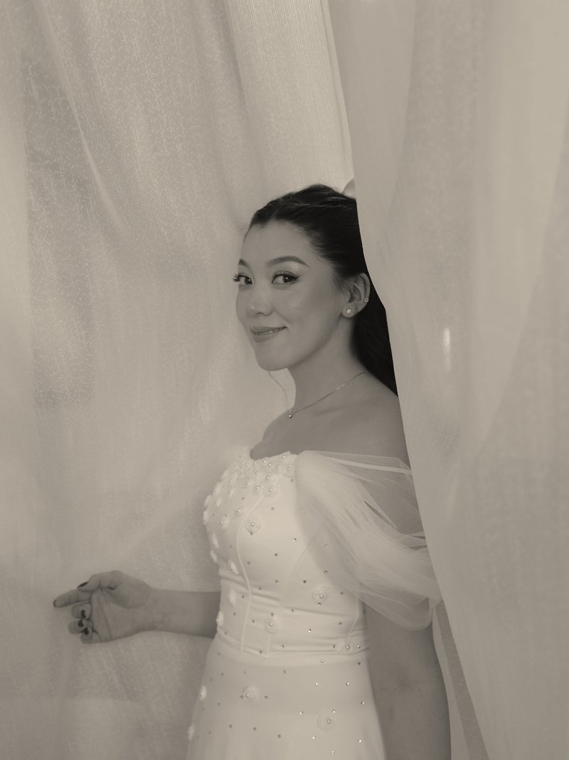 Bride in a white gown smiling from behind a sheer curtain